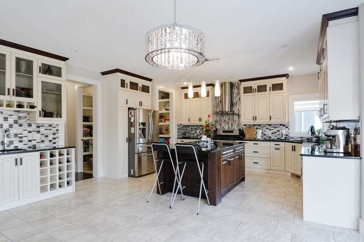 Kitchen with white ceiling, floor, walls and cabinets; dark wood island with steel/plastic stools; large chandelier overhead
