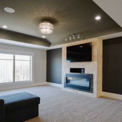 Upstairs TV room with light carpet, black, white and beige-stone walls; recessed ceiling with chandelier; dark sectional couch