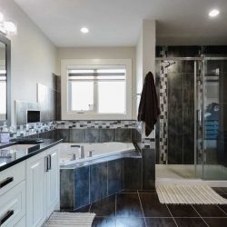 En suite bathroom with white walls and cabinets, black tile floor; window above corner tub, next two large shower