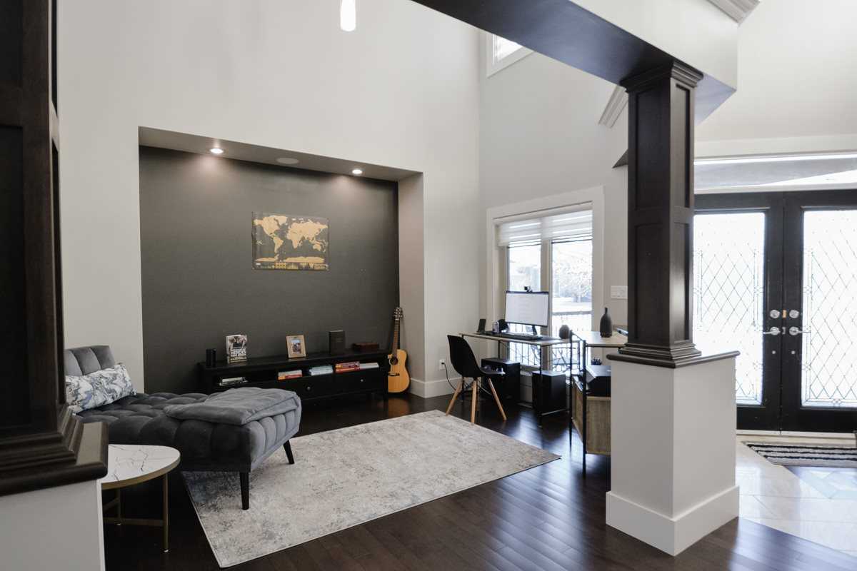 Interior home entrance, white walls with dark wood floor, doors and finishes; white rug, grey chaise lounge, acoustic guitar