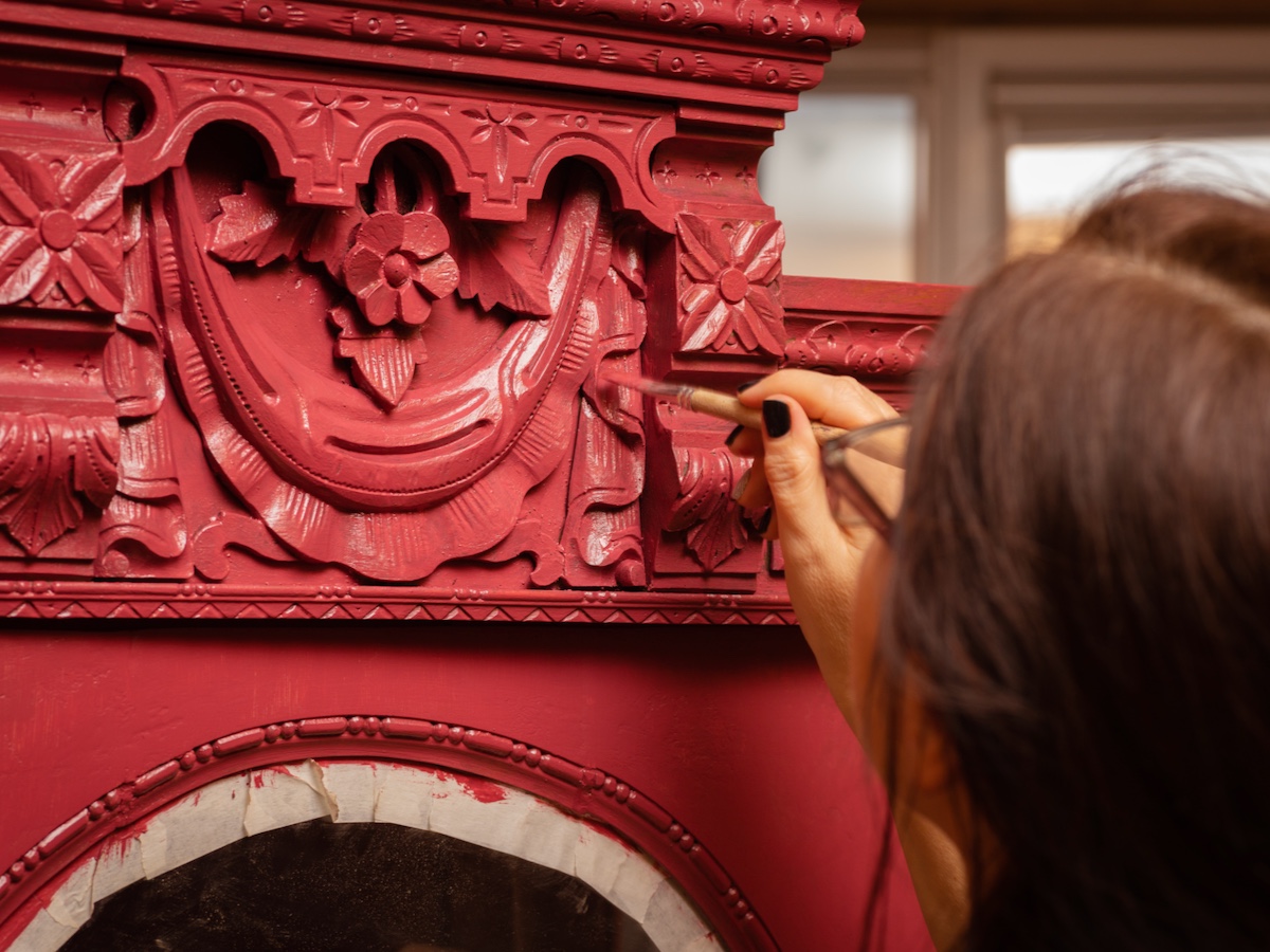 little brush in hand carefully painting old cupboard in pink red color.