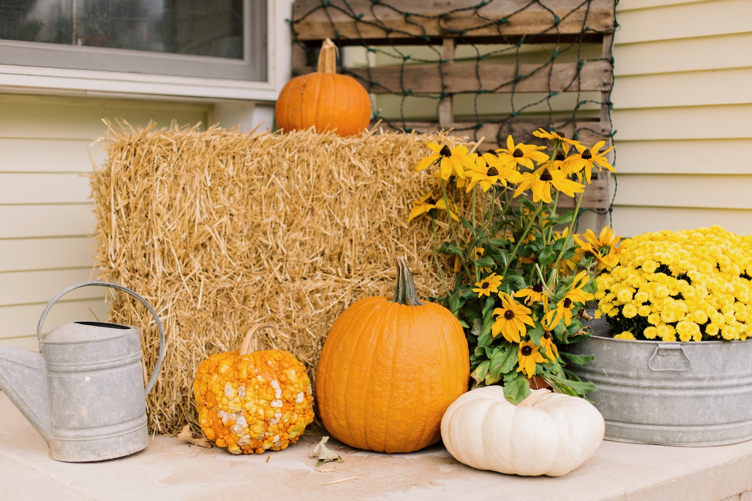 A decorative autumn front porch set up with pumpkins, gourds, mums, black eyed Susan’s, and a hay bale.
