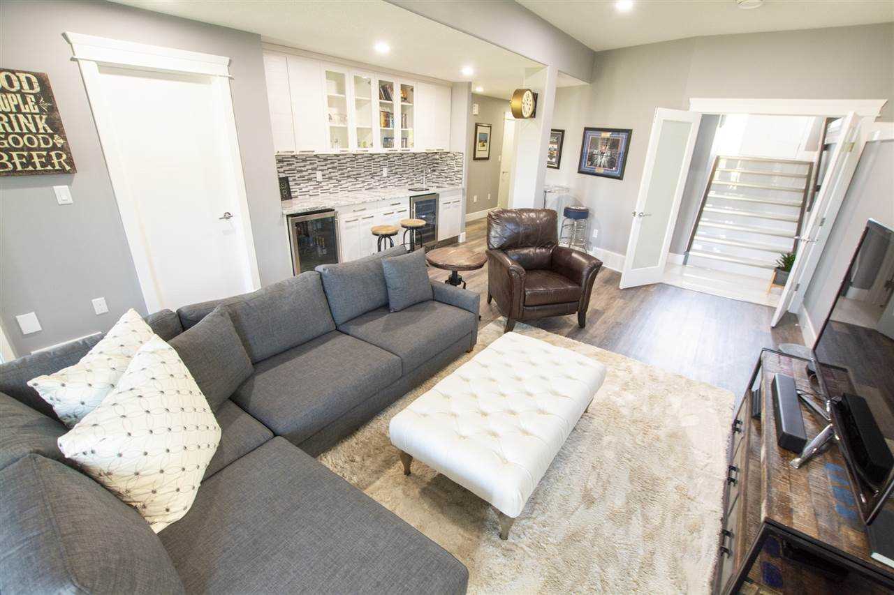 Basement with white walls, grey couch, wet bar in the background. 
