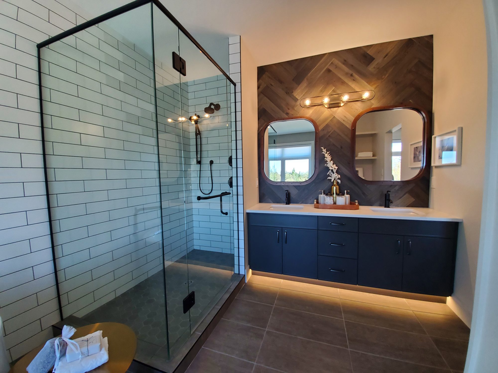 Large glass shower, dark tile floor, black cabinets, double sinks. 