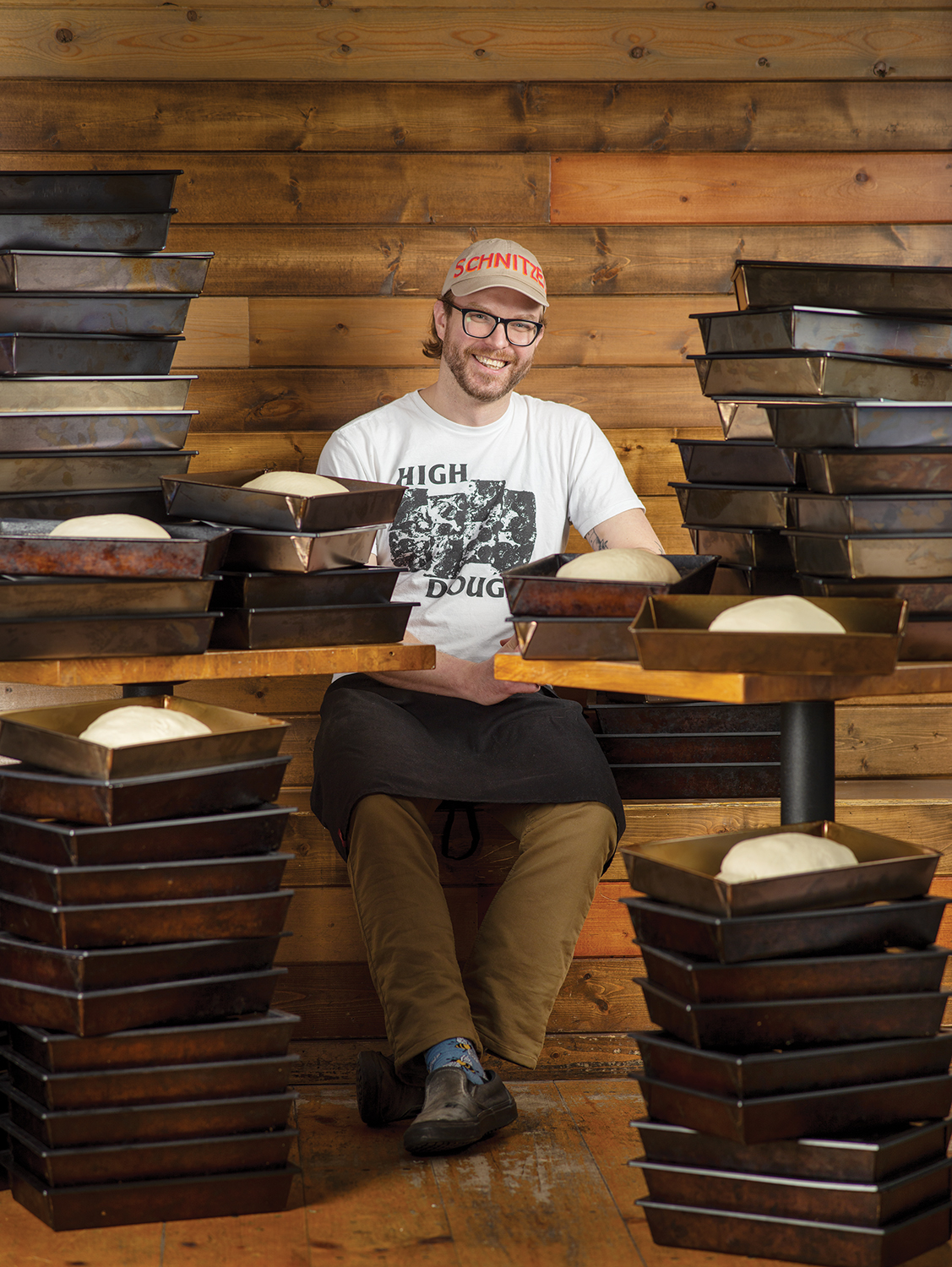 BraydenKozak_Sitting+LotsOfPansOfBreadsAroundHim_WoodBackground