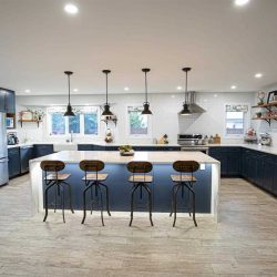 Kitchen with white ceiling and walls, light panel flooring, navy cabinets and white quartz waterfall island 