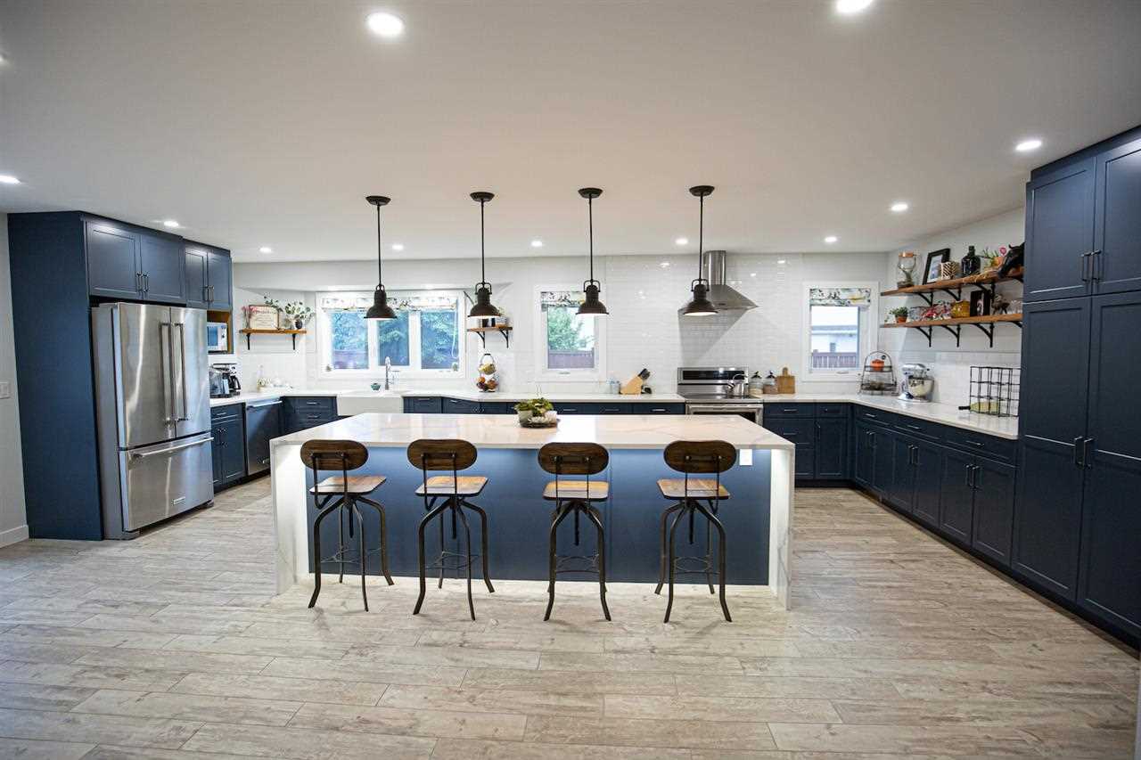Kitchen with white ceiling and walls, light panel flooring, navy cabinets and white quartz waterfall island 