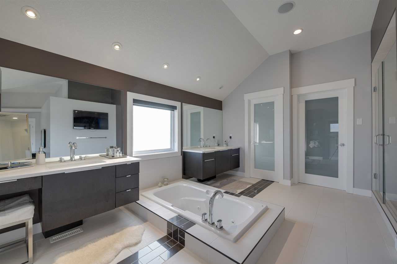 En suite, white ceiling, wall and floors with black trim; two sinks on either side of sunken soaker tub in front of window