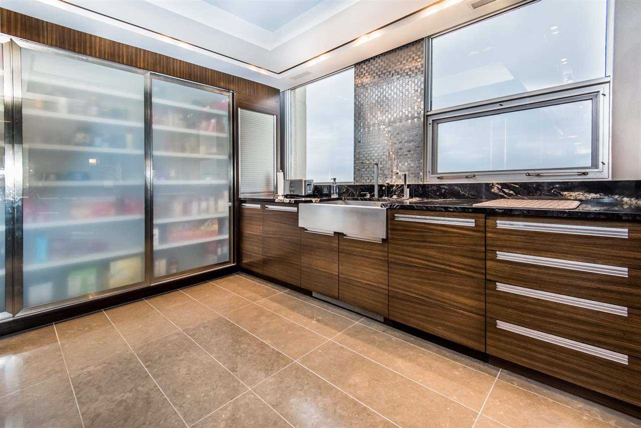 Interior kitchen with beige tile floor; black-with-white-splattered marble counter, steel backsplash in between frosted windows, above wood cabinets; frosted glass pantry doors on left