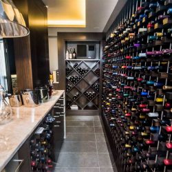 Wine room with grey tile floor; beige counter bar on left with decanters and steel chandelier on left; giant wall of wine on right