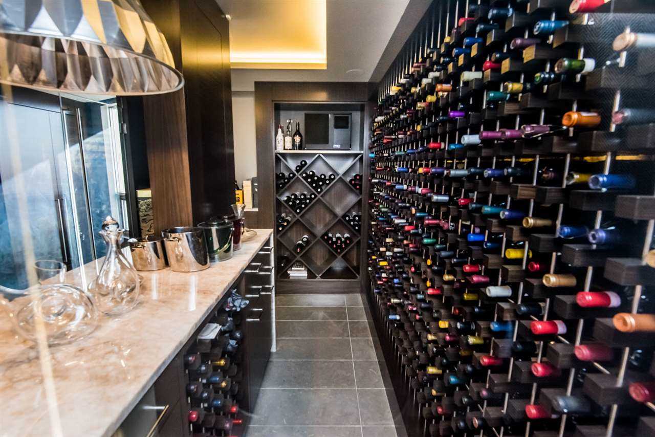 Wine room with grey tile floor; beige counter bar on left with decanters and steel chandelier on left; giant wall of wine on right