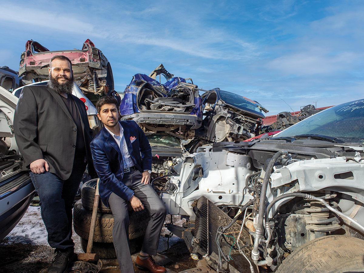 ChrisTrudelStanding_MikeZouhriSittingOnTires_WreckedVehiclesBehind_