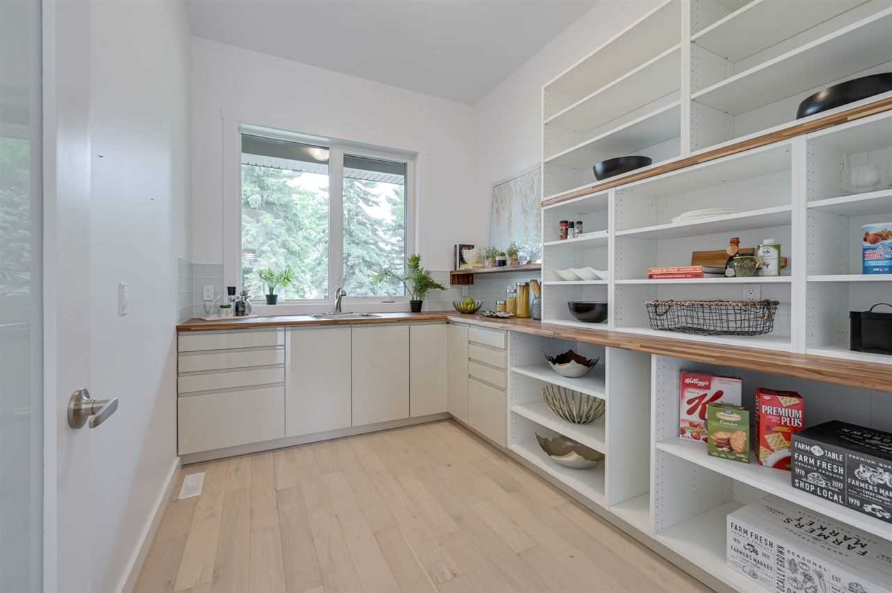 Butler pantry with large windows, sink and floor-to-ceiling shelves. White walls and white oak floor