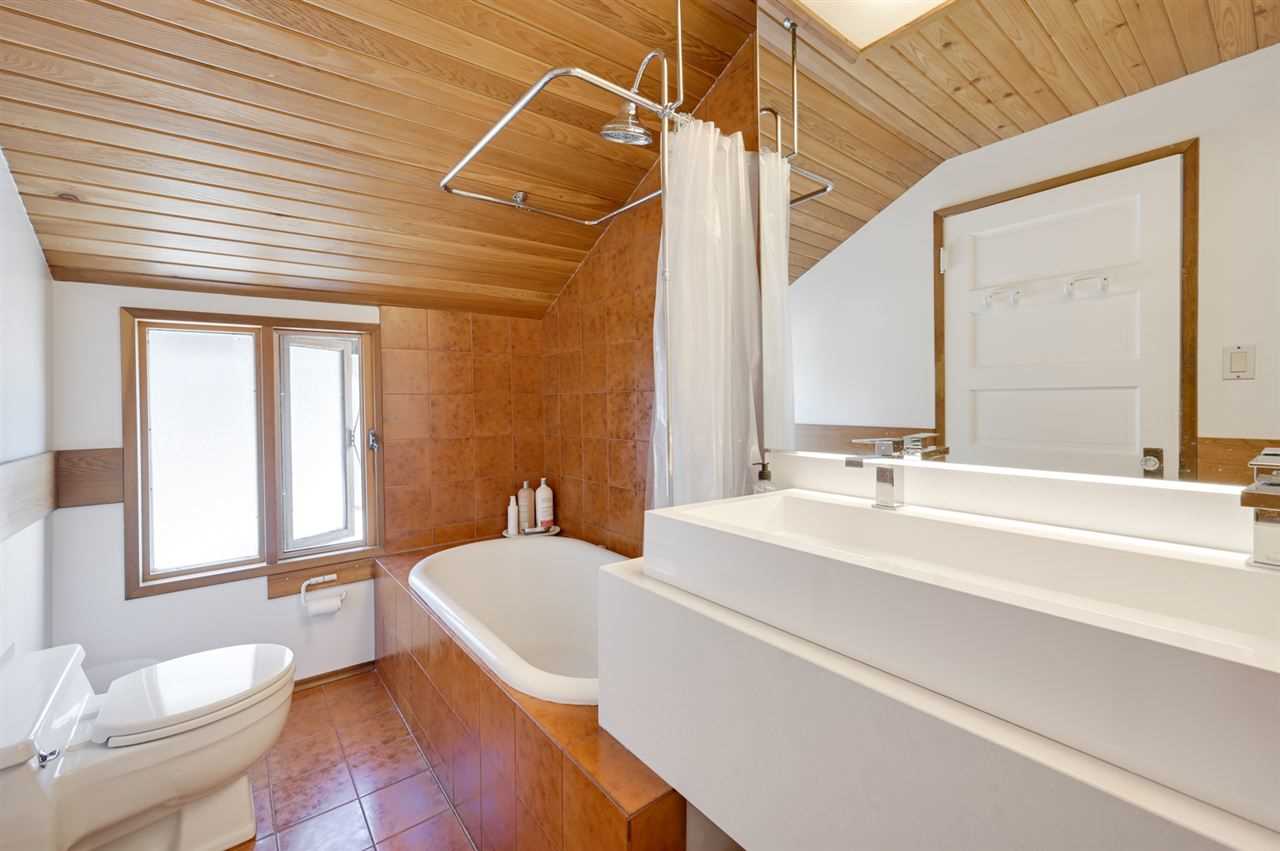 Wood floor, ceiling and walls; white sinks, toilet and tub with free-hanging curtain. 
