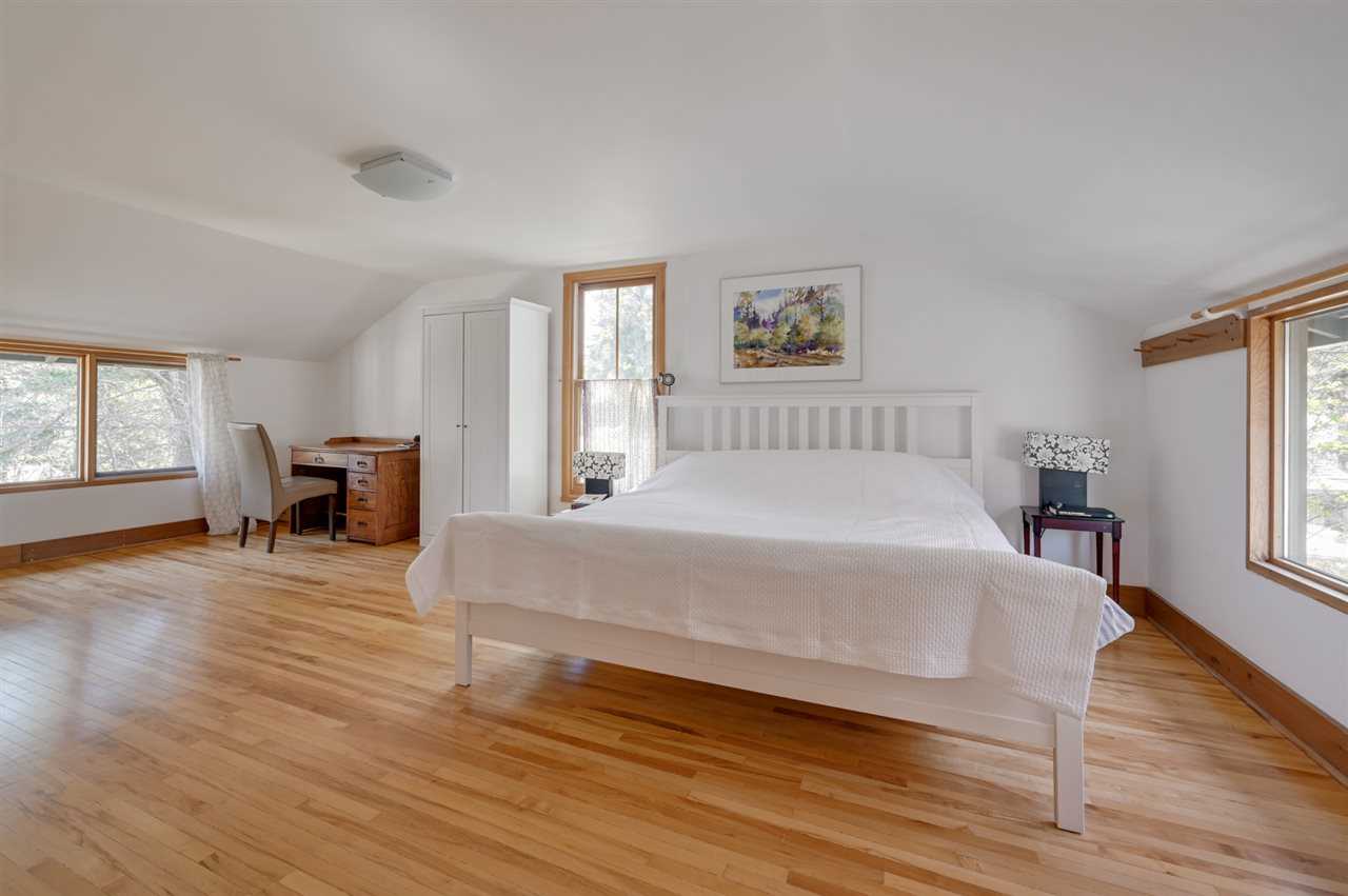 Wood floor, white walls, white bed, a window on each of three walls.