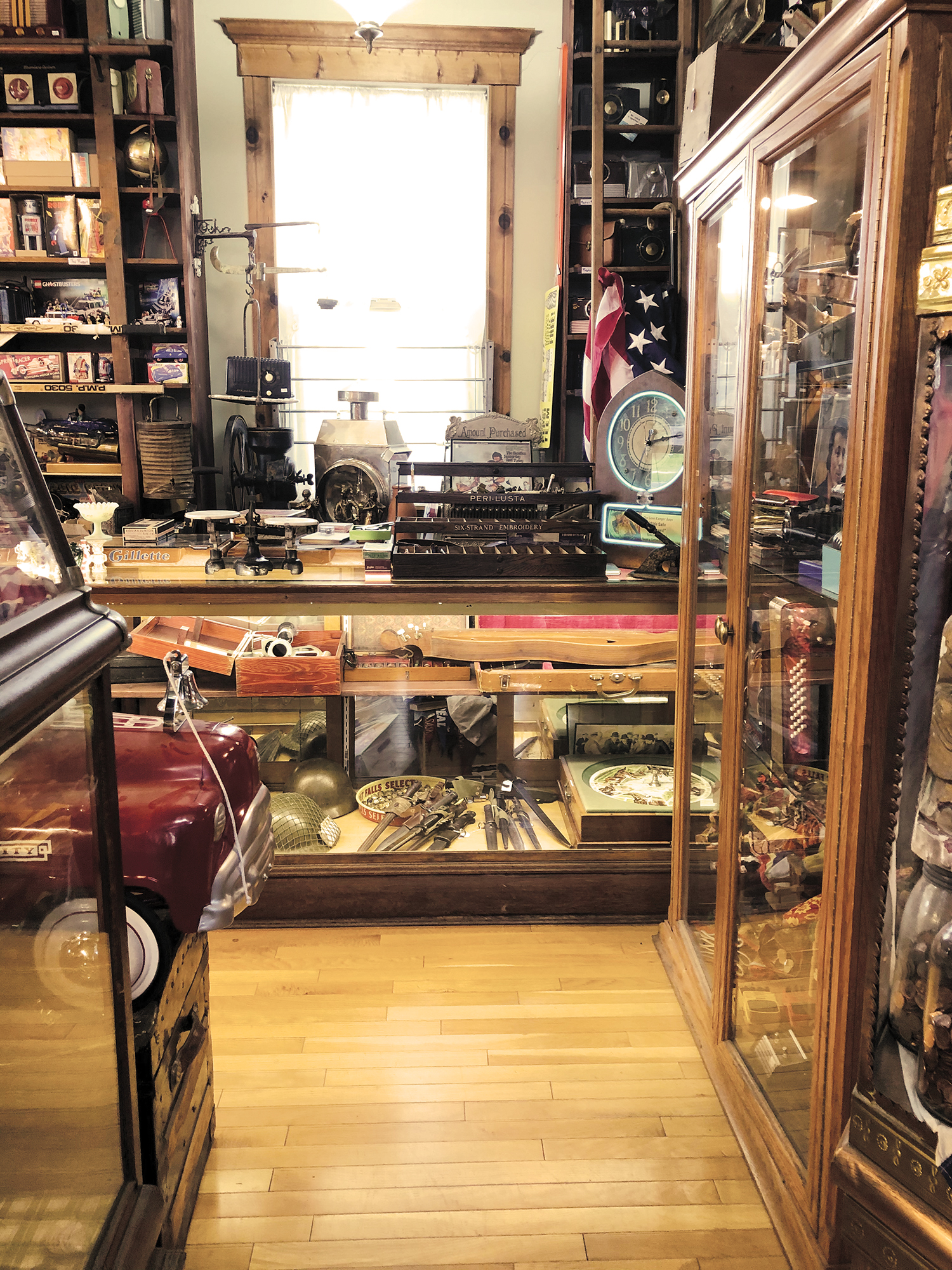 Antique store, wood floor, glass case and cabinet, wood framed window, front end of dark red model car. Antique store, wood floor, glass case and cabinet, wood framed window, front end of dark red model car.