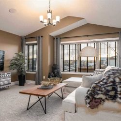 Upstairs bonus room with peaked ceiling and large windows and grey curtains; light grey carpet, white couch with black and white animal pattern blanket; wood coffee table
