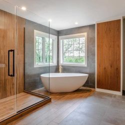 En suite bathroom with white ceiling, tile floor on right, wood floor on left leading to glass-wall shower lined with wood; white soaker tub in windowed corner