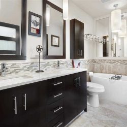 En suite bathroom, white floor, ceiling, walls and counter; black cabinets; two rectangular sinks; white tub on right