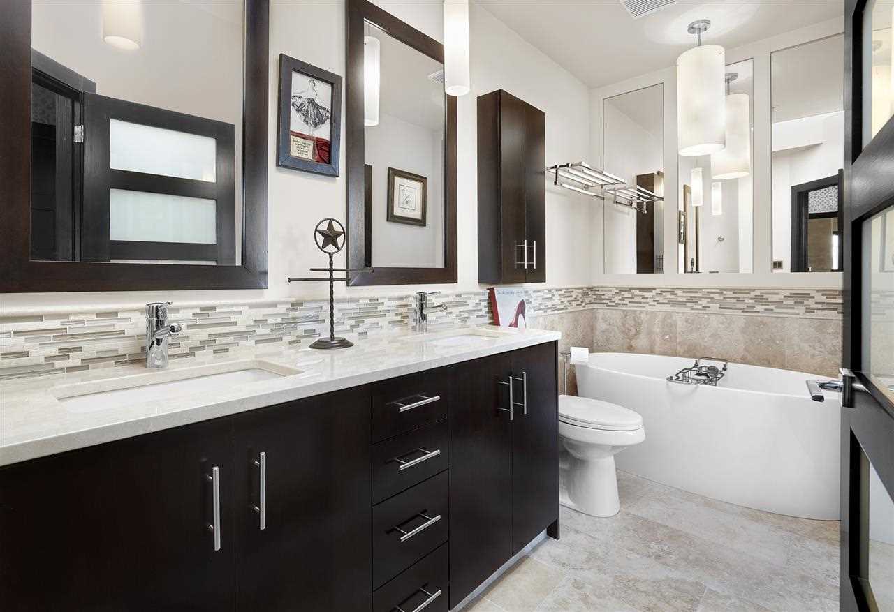 En suite bathroom, white floor, ceiling, walls and counter; black cabinets; two rectangular sinks; white tub on right