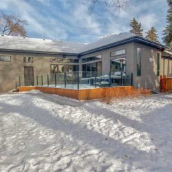 Exterior backyard in winter; wood deck with glass rails extends of grey bungalow