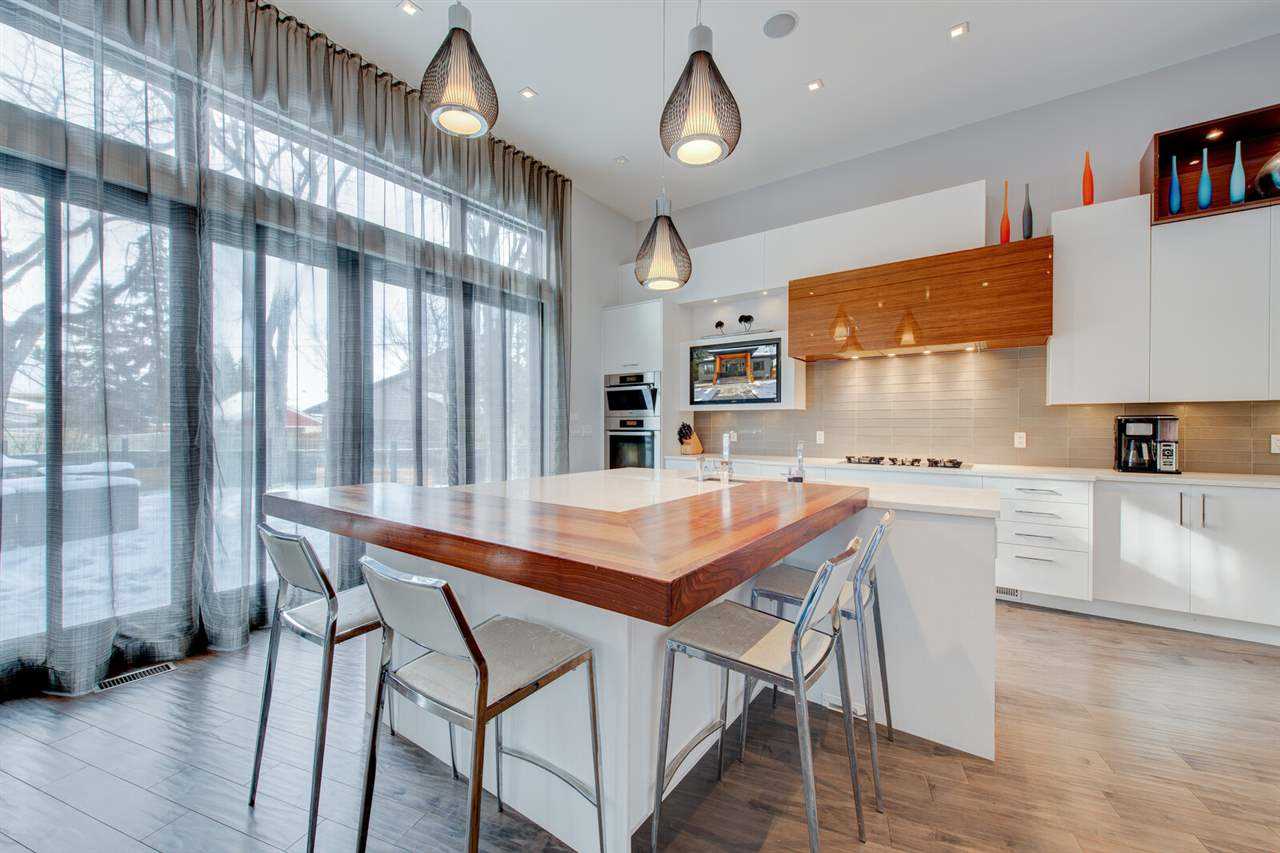 Kitchen with hardwood floor, white cabinets, ceiling and walls; rectangular wood extension off white island with sink; three stools around it, three hanging lights above