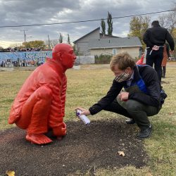 A man spray painting a statue of a man squatting down