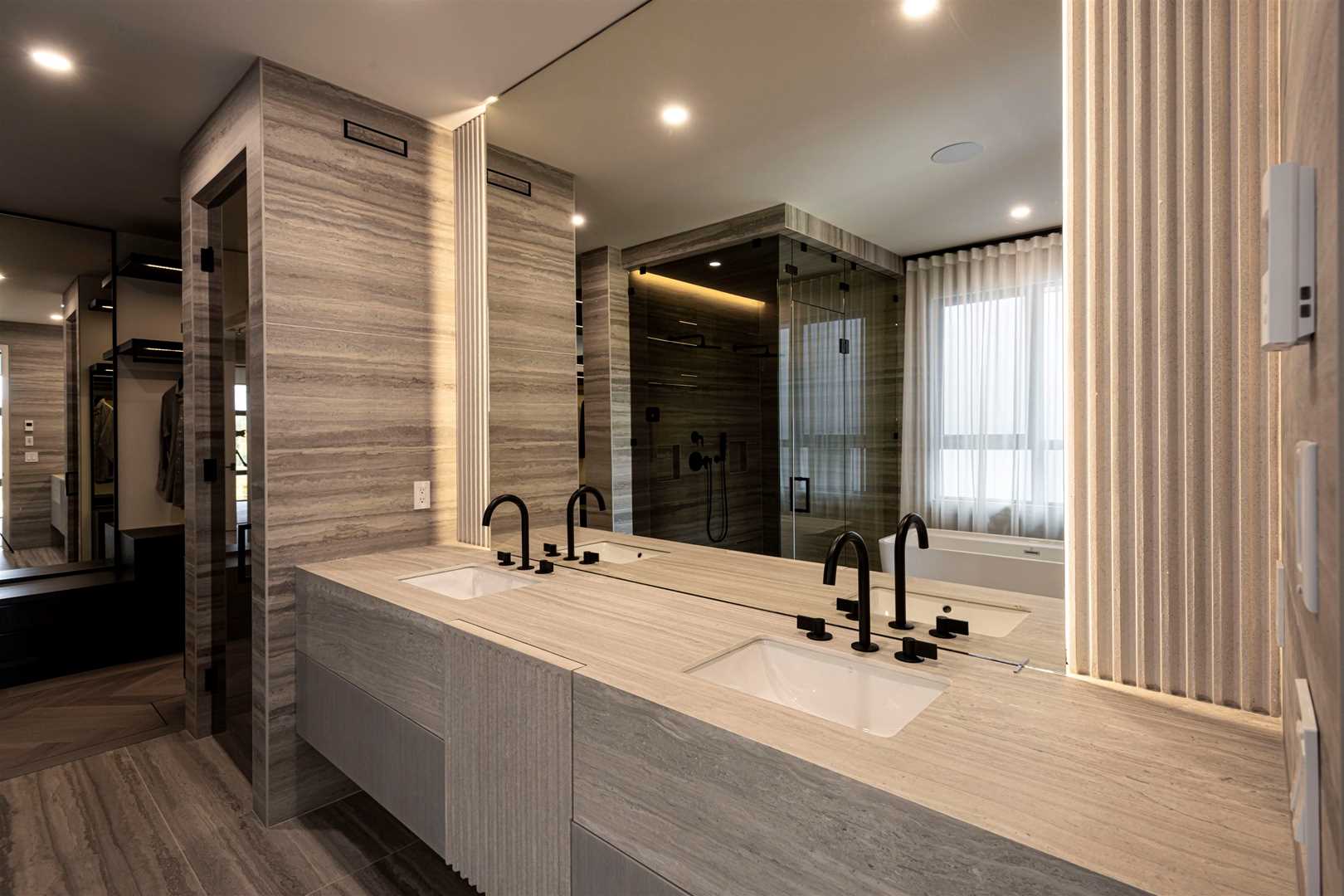 En suite bathroom, light, textured laminate floor with matching counter and walls; two sinks in front of large mirror, shower and closet to left