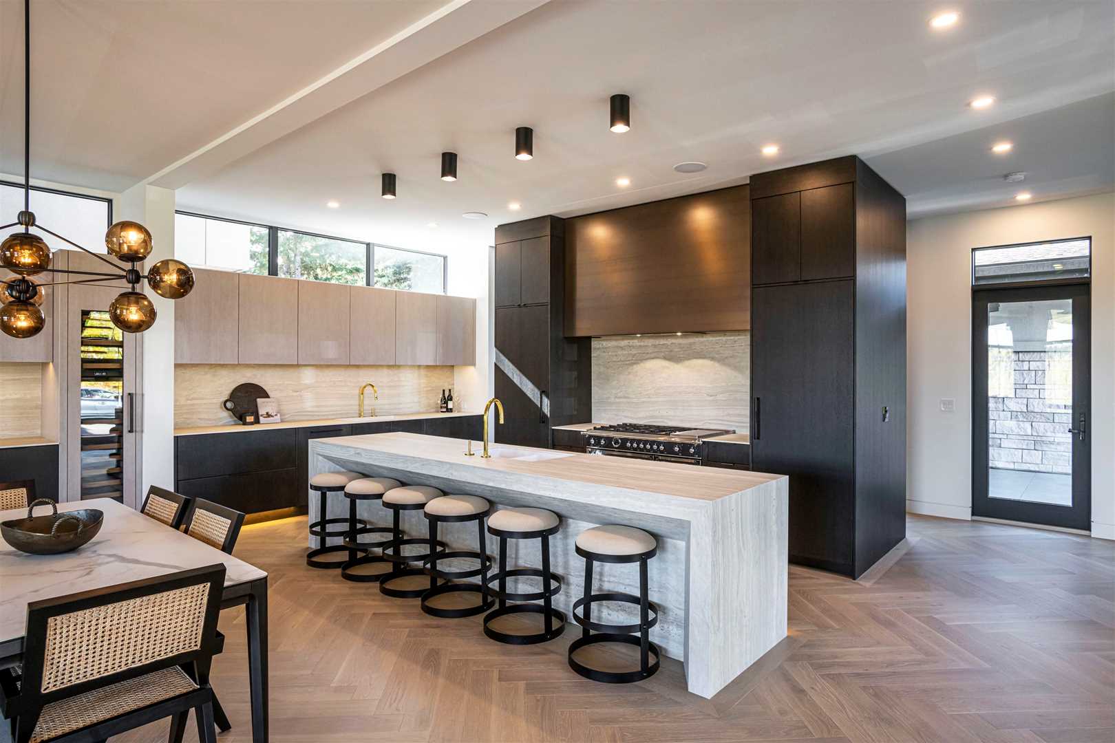 Kitchen with light hardwood floor, white ceiling; white marble waterfall island with six chairs facing black bordered stove area