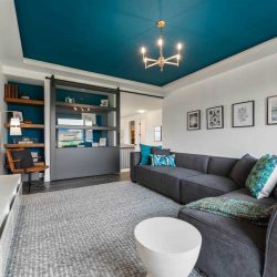 Upstairs bonus room with white walls and turquoise ceiling; chandelier and light grey carpet; bookshelf and wall-mounted TV
