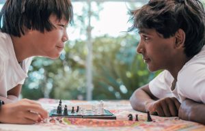 two boys of indian and chinese origin stare into each other's eyes while playing chess. concept of competitiveness and racial diversity.
