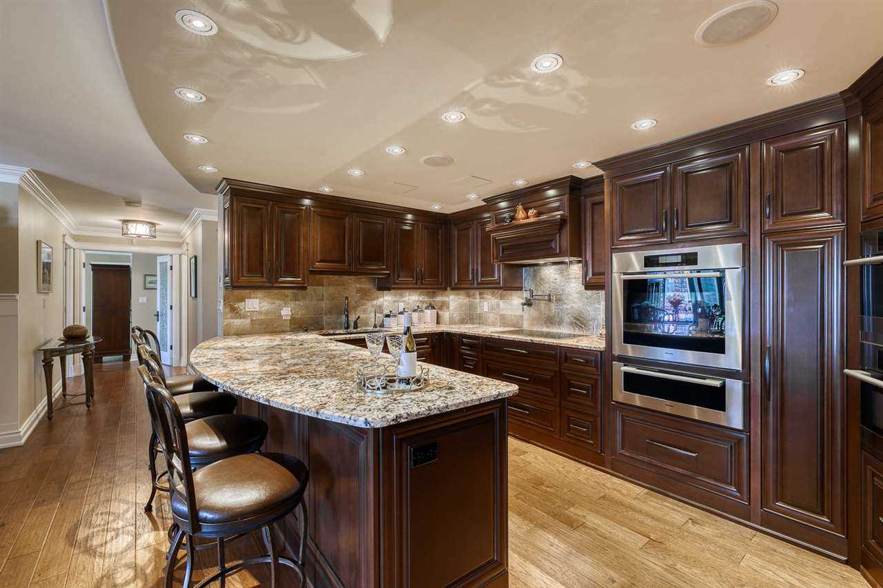 Kitchen with hickory hardwood floor, dark wood cupboards and cabinets, light ceiling with embedded lights, light marble countertops; island in foreground, rounded on seating side with four stools