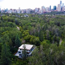 Exterior shot of three-storey home surrounded by green trees and Edmonton skyline in the background