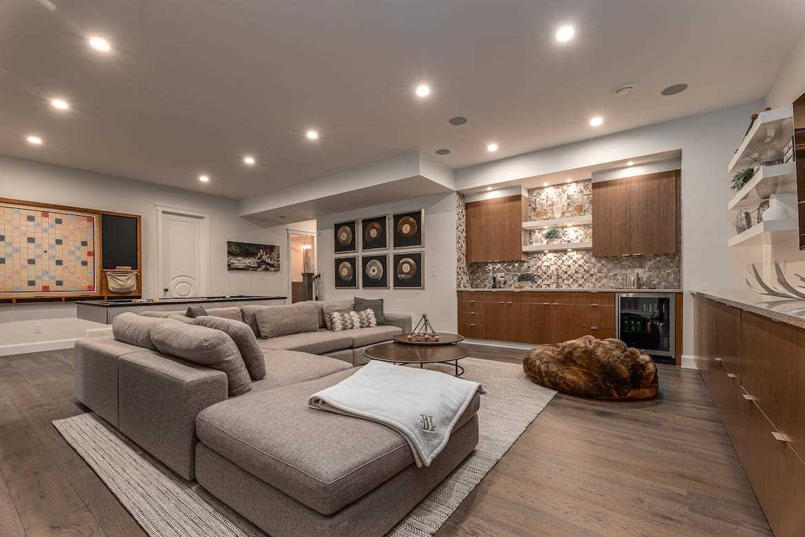 Grey couch, light brown hardwood floor, brown cabinets, embedded ceiling lights. 