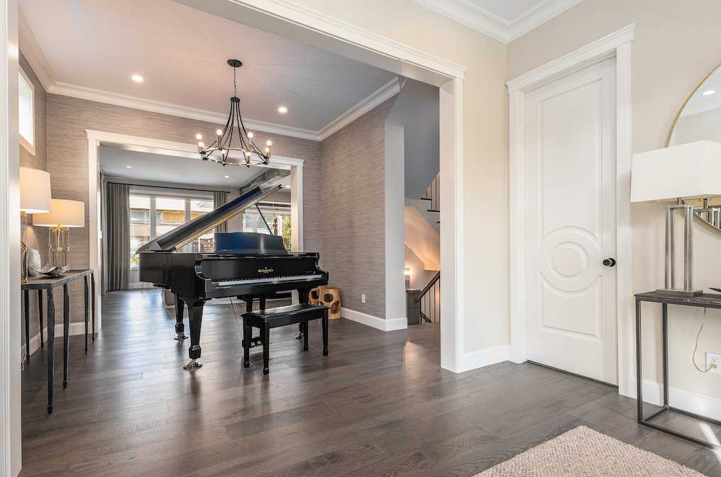 Front entrance, white walls, muted grey floors, black grand piano, chandelier. 