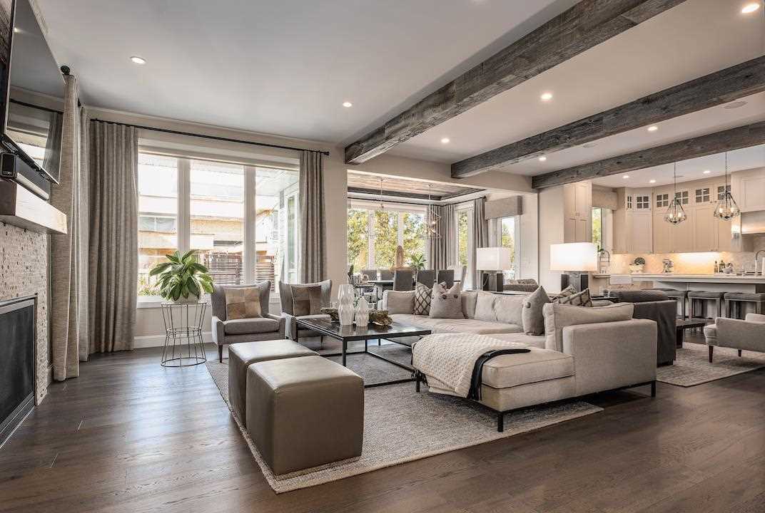 Grey floors, grey ceiling beams, light grey couches, wall-mounted TV above fireplace.