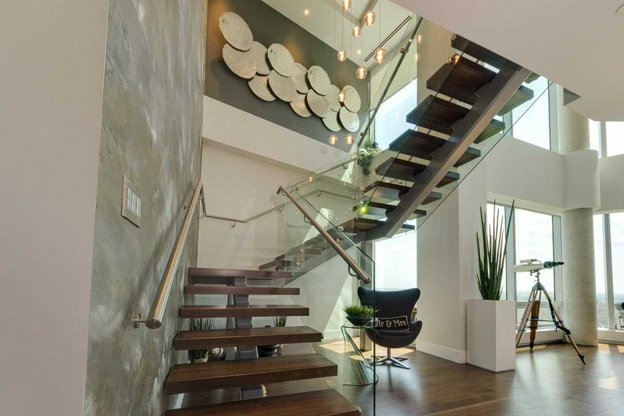 Interior open-air staircase; wood stairs, steel railing; silver textured wall on left; artwork with repeating circles on landing wall; chair underneath the stairs
