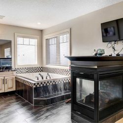 En suite bathroom with dark floors, corner bathtub, three-sided fireplace and wall-mounted TV