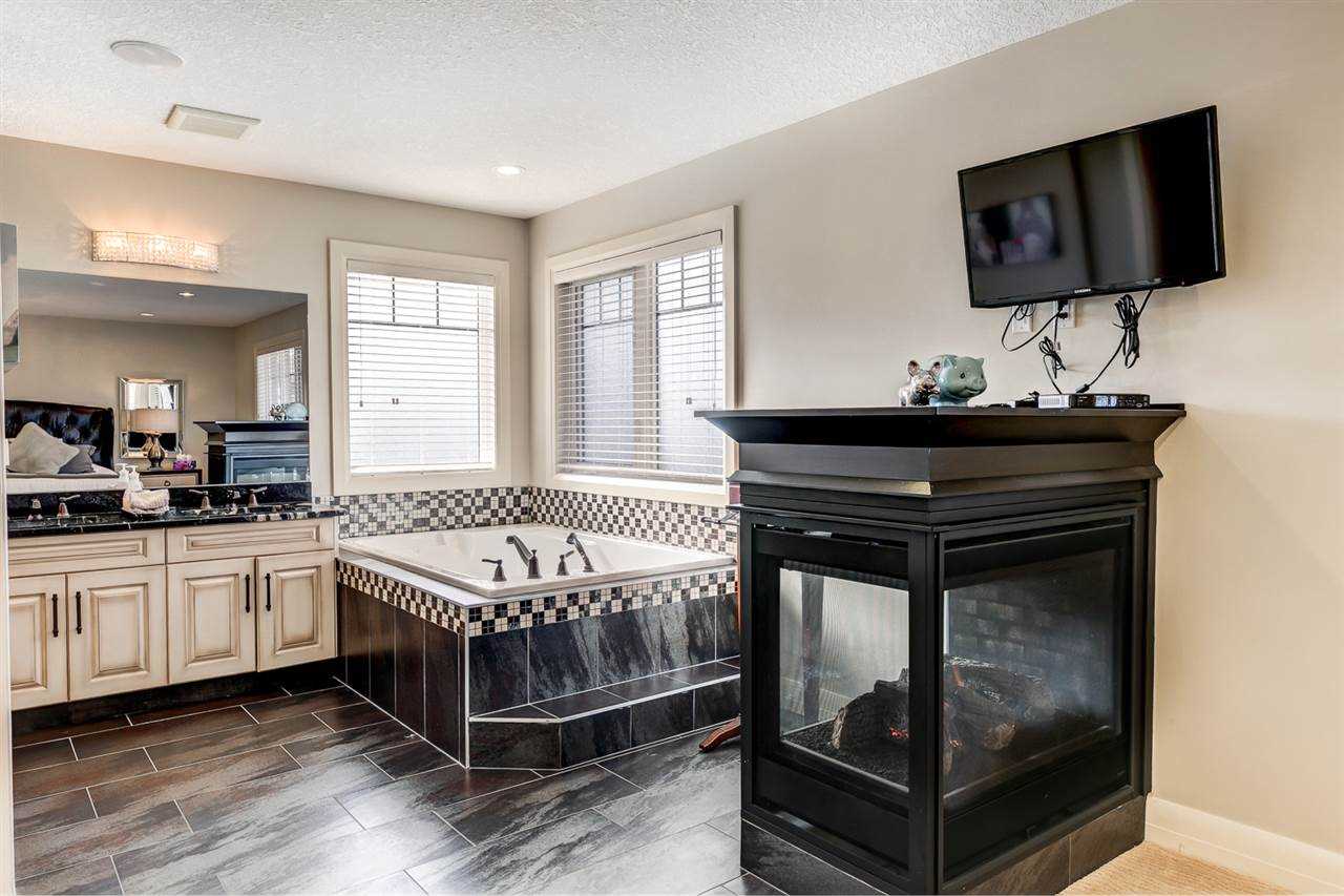 En suite bathroom with dark floors, corner bathtub, three-sided fireplace and wall-mounted TV