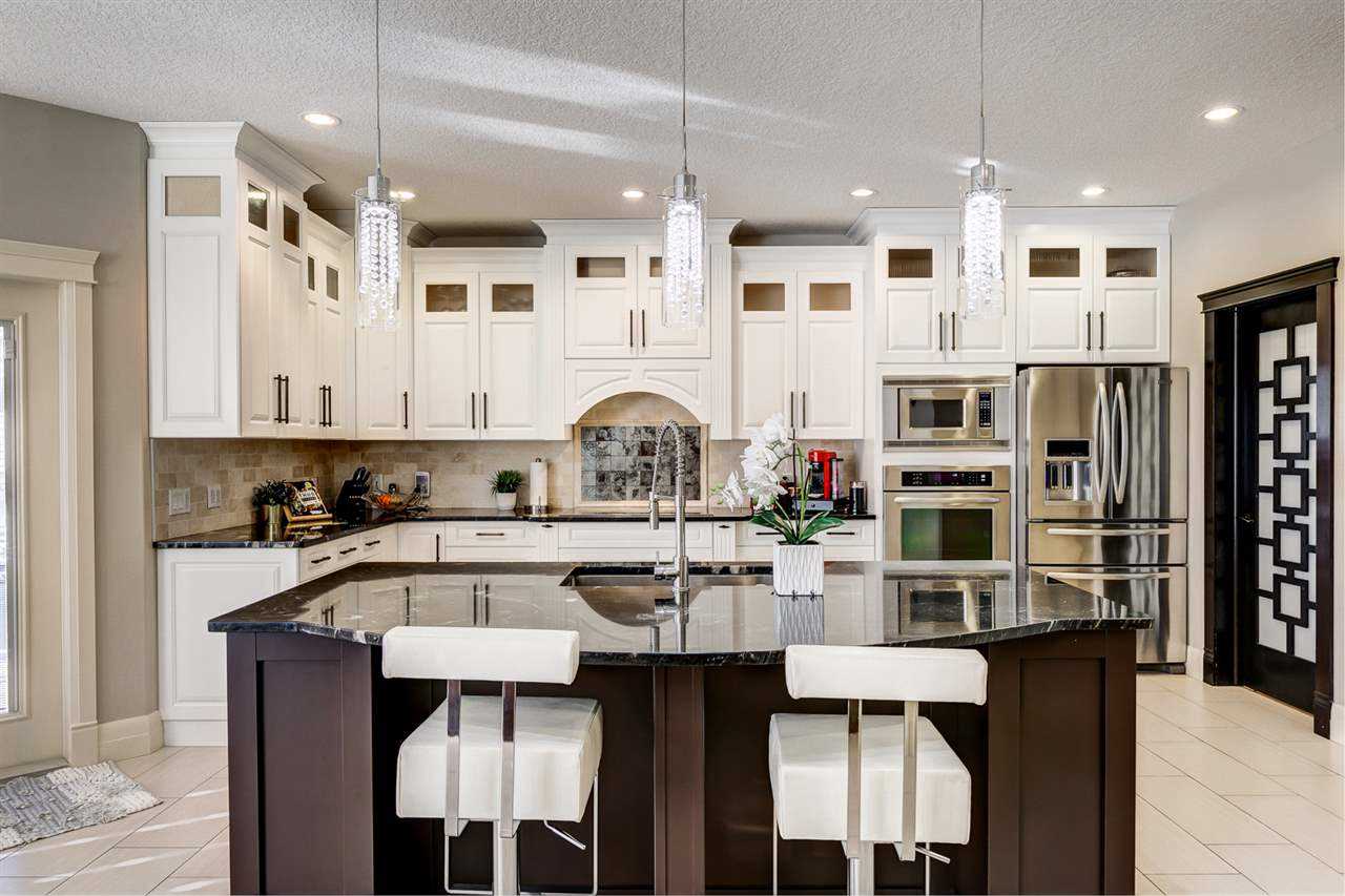 Kitchen with white cabinets, three lights hanging over black island with white chairs