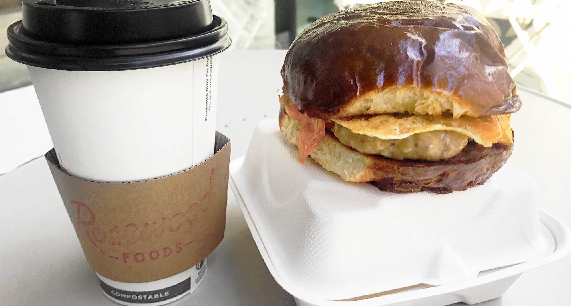 chicken sausage and egg breakfast sandwich with milk bun and a side of take-out coffee