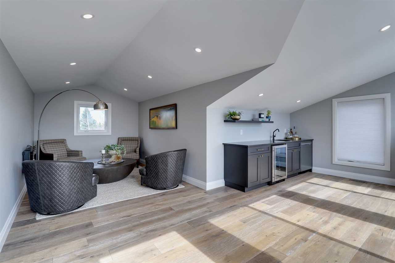 Upstairs loft, white ceiling and walls, light hardwood floor; four black chairs to left around half-sphere coffee table; small sink, mini-fridge and washer to right