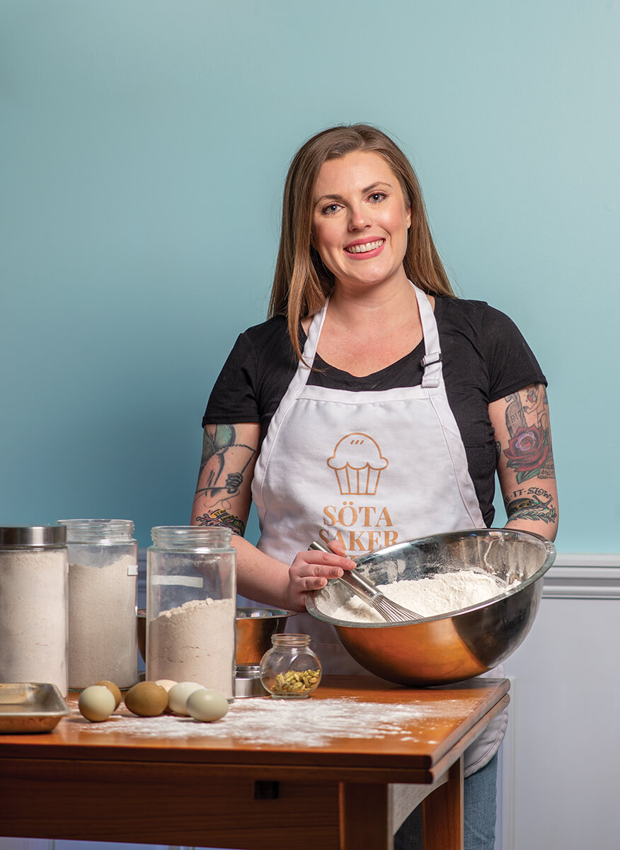 Sota_Saker_JennaMarsh_StandingBehindIsland_WhiteApron_WhiskingFlour_MetalBowl