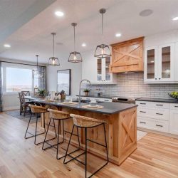 Kitchen, with white ceiling and light wood floor; light wood base for kitchen island with three lights hanging over it; white cabinets