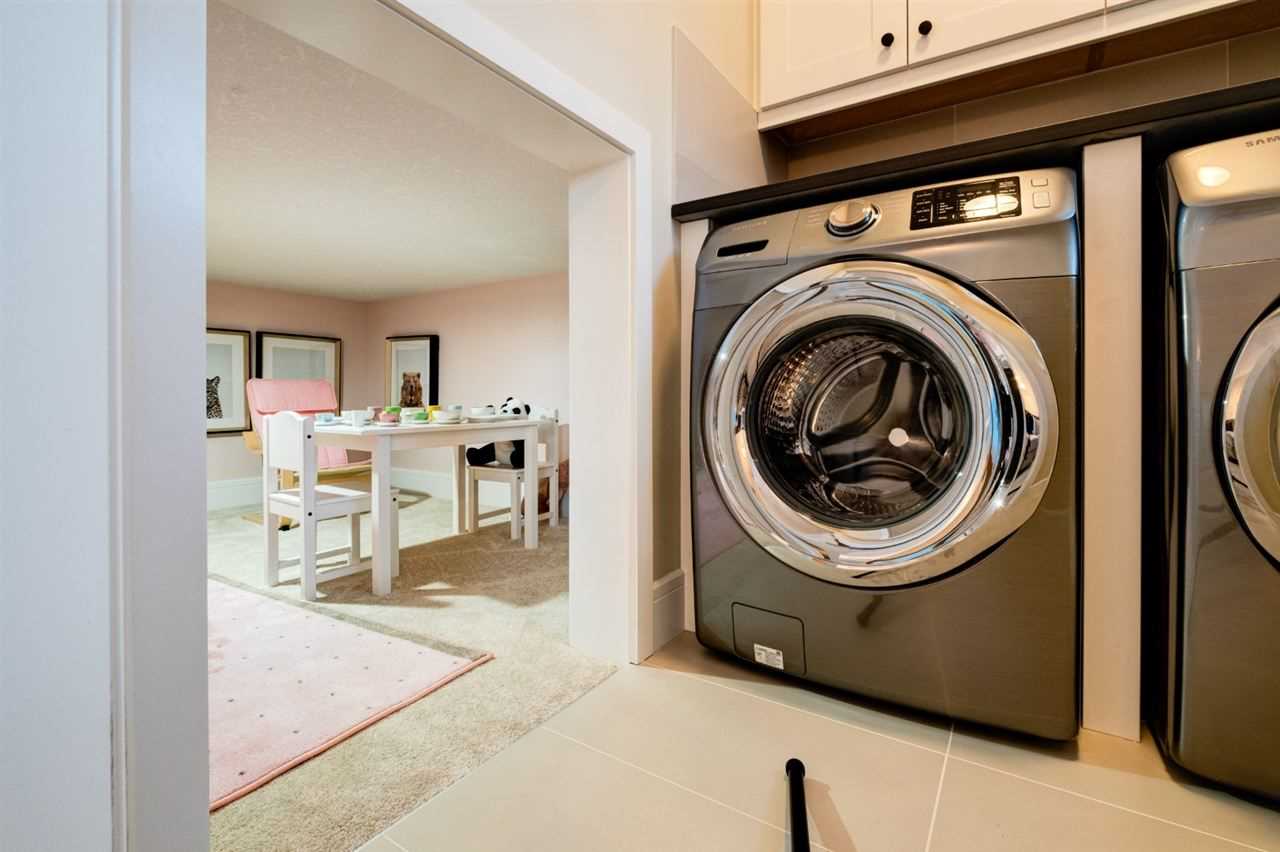 Laundry room, with grey and silver clothes dryer, opening to a half-height kids' crawl space with tea party decor