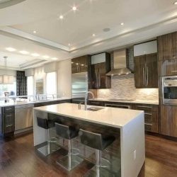 Interior kitchen with white ceiling, matching dark wood floor and cabinets; white countertops and island with sink and three stools