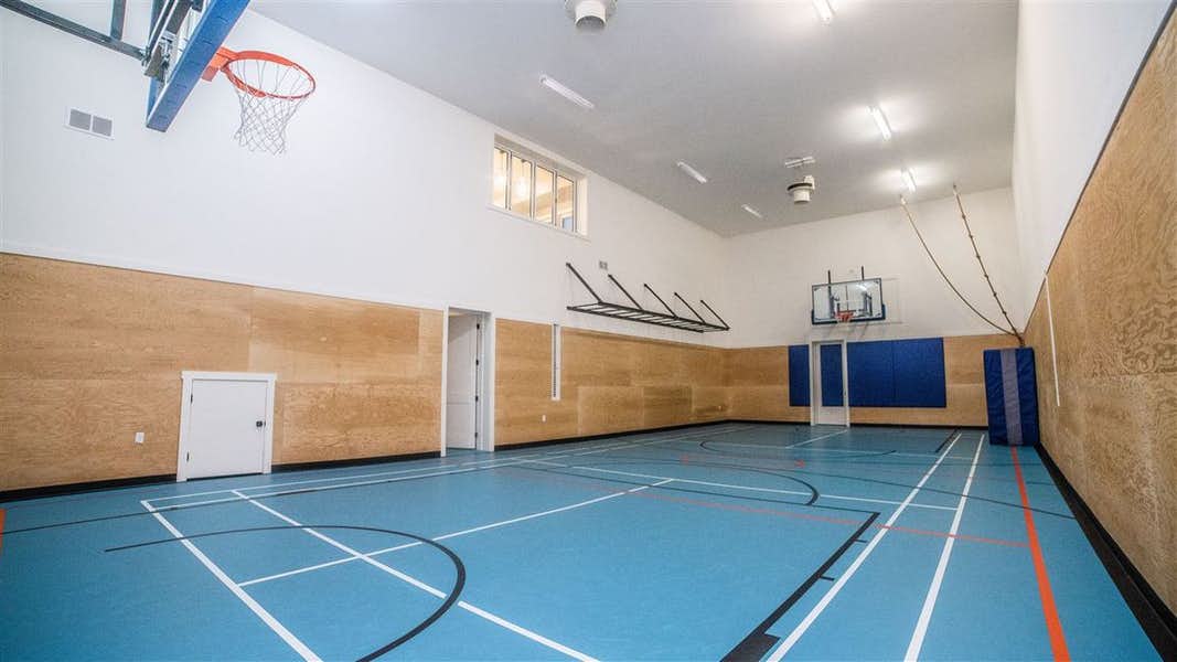 Interior basketball court with blue floor, light wood panelling on bottom half of white wall; windowed viewing area on top left