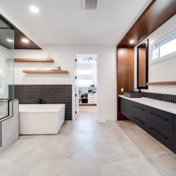 En suite bathroom, white ceiling and walls, light hardwood floor; large mirror over white counter and black cupboards on right; shower and soaker tub on left