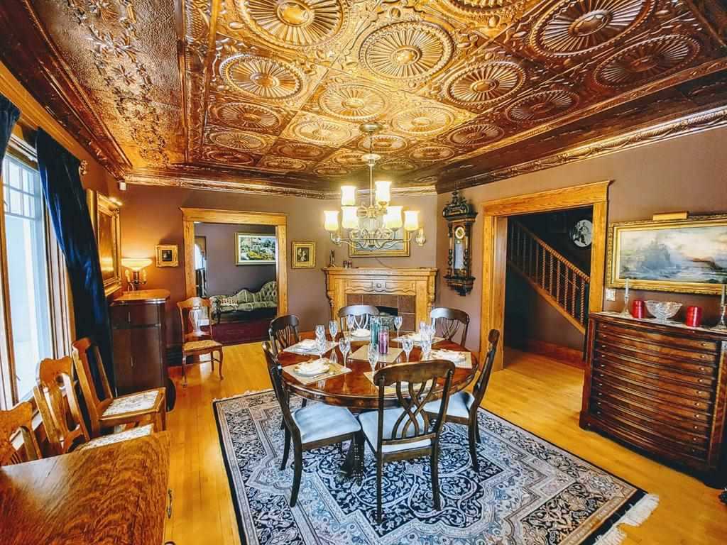 Interior dining room with wood floor and walls, and decorative ceiling panels above; circular wood table with six wood chairs around, on top of navy and white pattern rug; wood cabinets on the right and left, fireplace on back wall