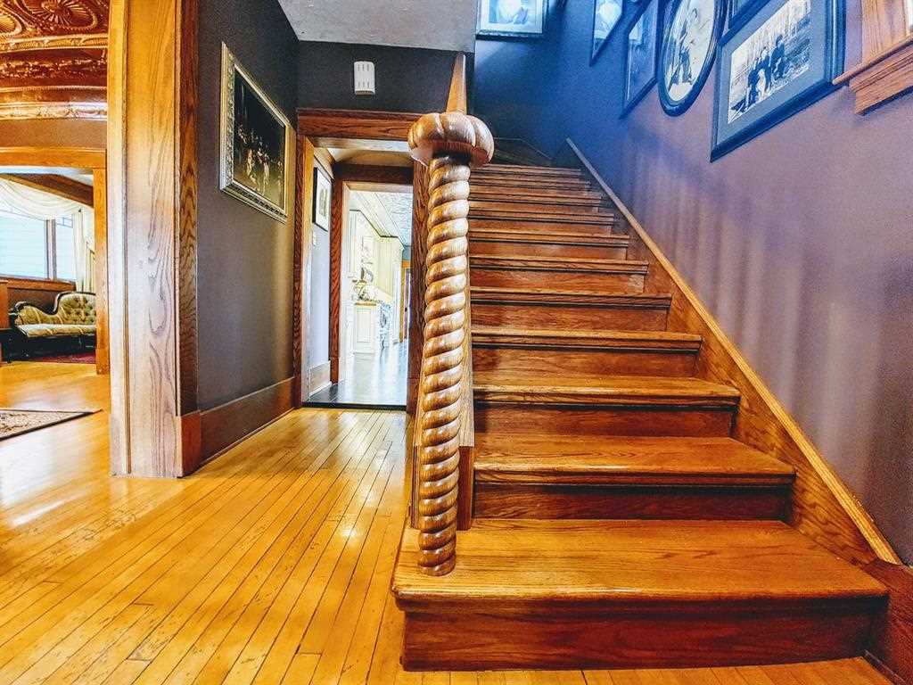 Interior entrance looking at hand-crafted wood stairs with a spiral post railing at the bottom; hardwood flooring leading to kitchen straight ahead, and to living room on the left